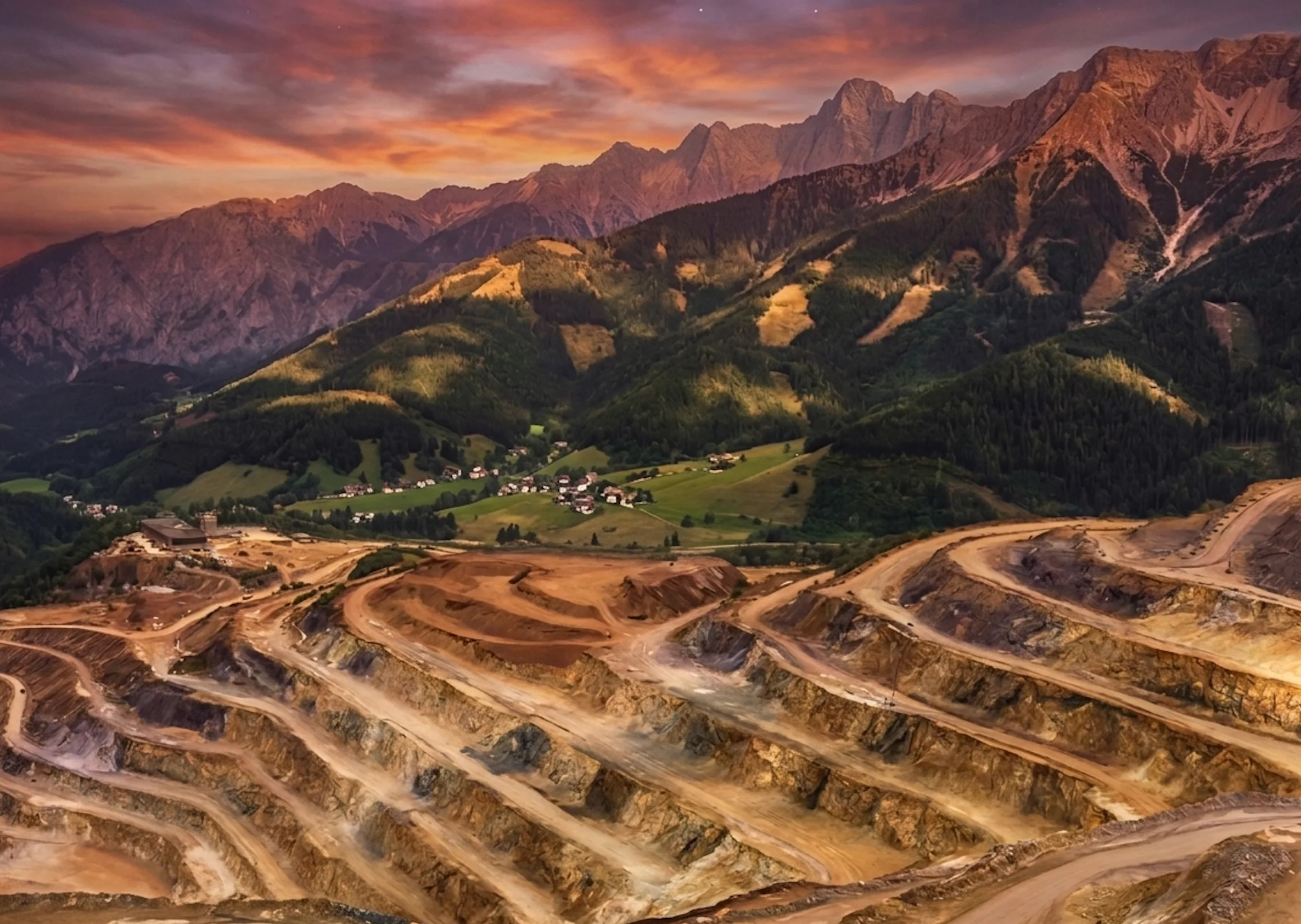 Open-pit rare-earth mine terraced into a mountainside at dusk